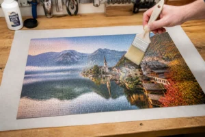 Application de colle spéciale puzzle sur un puzzle de 1000 pièces avec un pinceau plat, fond atelier bois