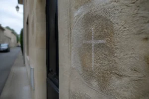 Trace de craie en forme de croix sur un mur de pierre près d'une porte d'entrée, lumière naturelle