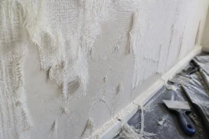Dépose de toile de verre sur un mur ancien, filaments arrachés et plâtre dégradé visible